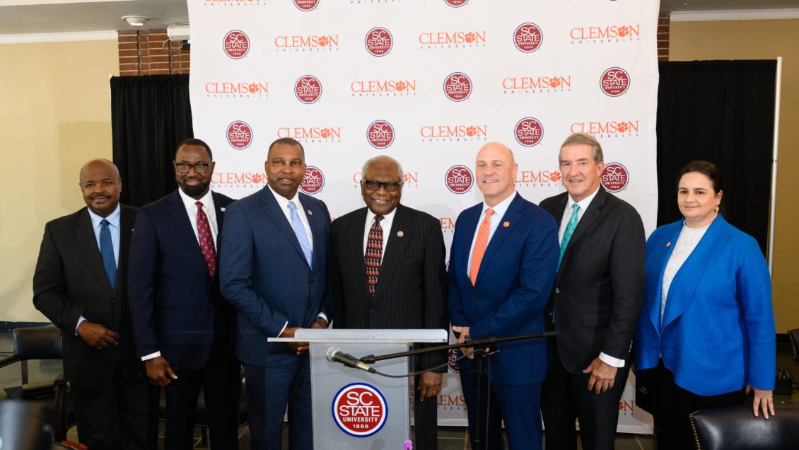 Dignitaries from South Carolina State University, Clemson University, the state of South Carolina and U.S. Congress stand in front of a banner with Clemson and S.C. State logos