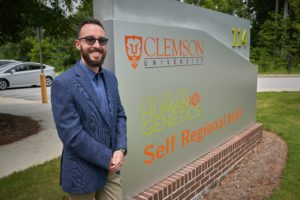 Man wearing a suit and sunglasses stands in front of a sign at the Clemson University Center for Human Genetics