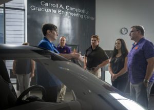 Students gather around a car at CU-ICAR to listen to a speaker standing next to the vehicle speak.