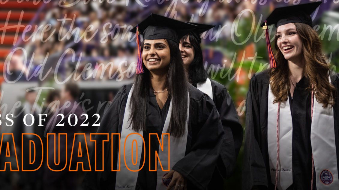 Two female students wearing graduation caps and gowns walk toward the stage at a commencement ceremony. A text overlay reads, “Class of 2022 Graduation,” and lyrics to the University’s alma mater are displayed in the background.