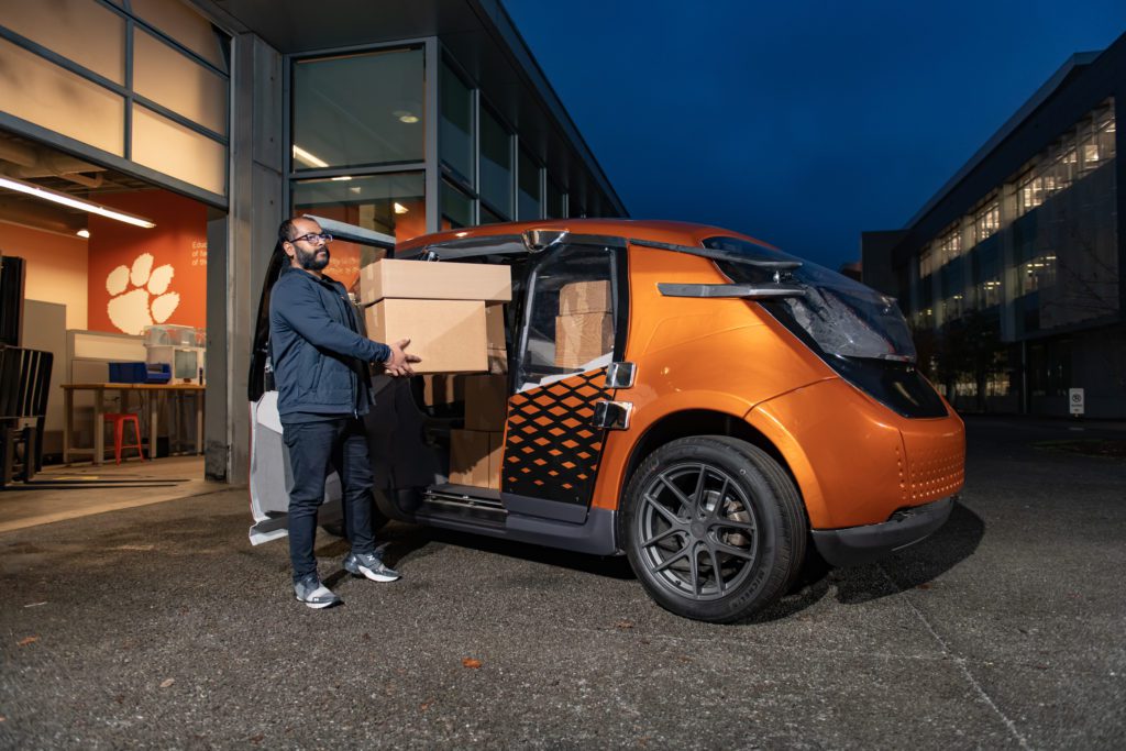 A man loads cardboard boxes into an orange car. 