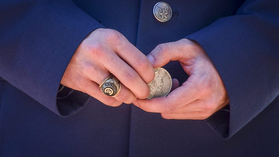 A close-up of the waist of a man, wearing military dress blues, holds a silver dollar in his hands ready to participate in the Second Lieutenants joint commission ceremony. His Clemson University class ring is worn on his right hand.