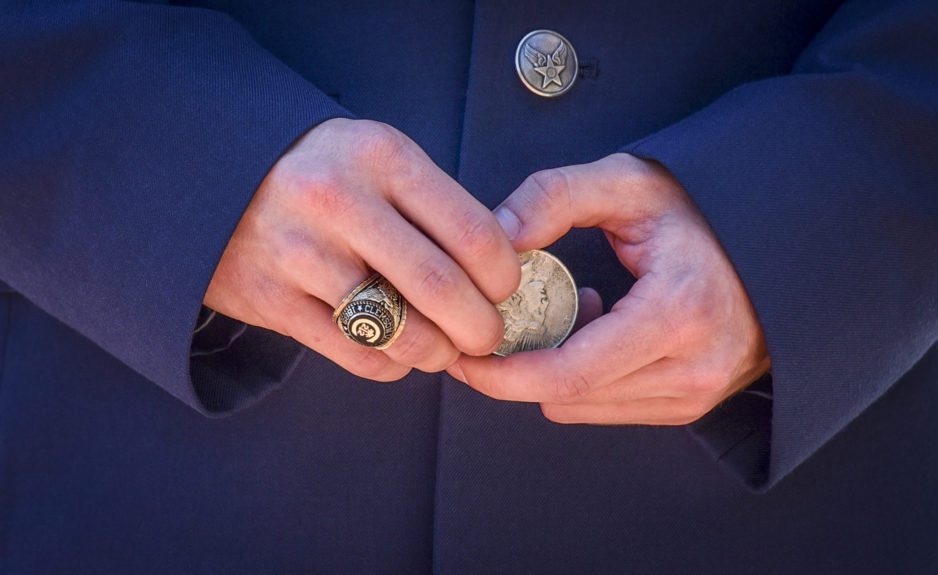 A close-up of the waist of a man, wearing military dress blues, holds a silver dollar in his hands ready to participate in the Second Lieutenants joint commission ceremony. His Clemson University class ring is worn on his right hand.