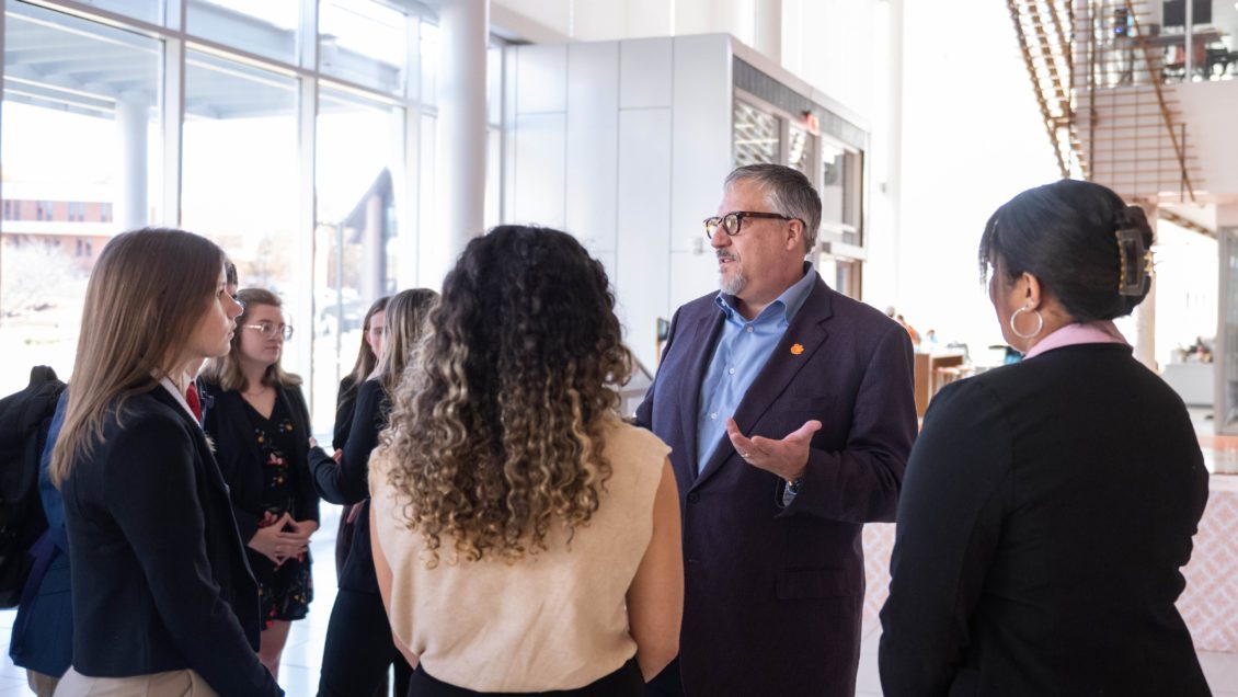 A middle-aged man, TransDigm President and CEO Kevin Stein, is conversing with a group of mostly female students who are recepients of the Doug Peacock Scholarships.