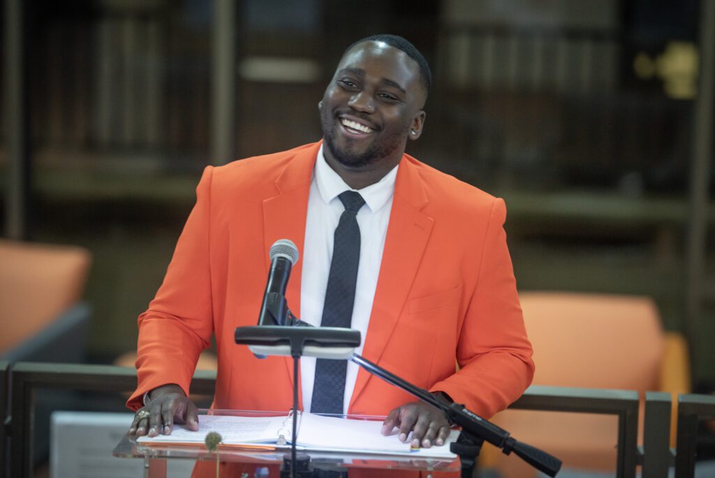 A young man in a Clemson orange suit coat speaks from a podium