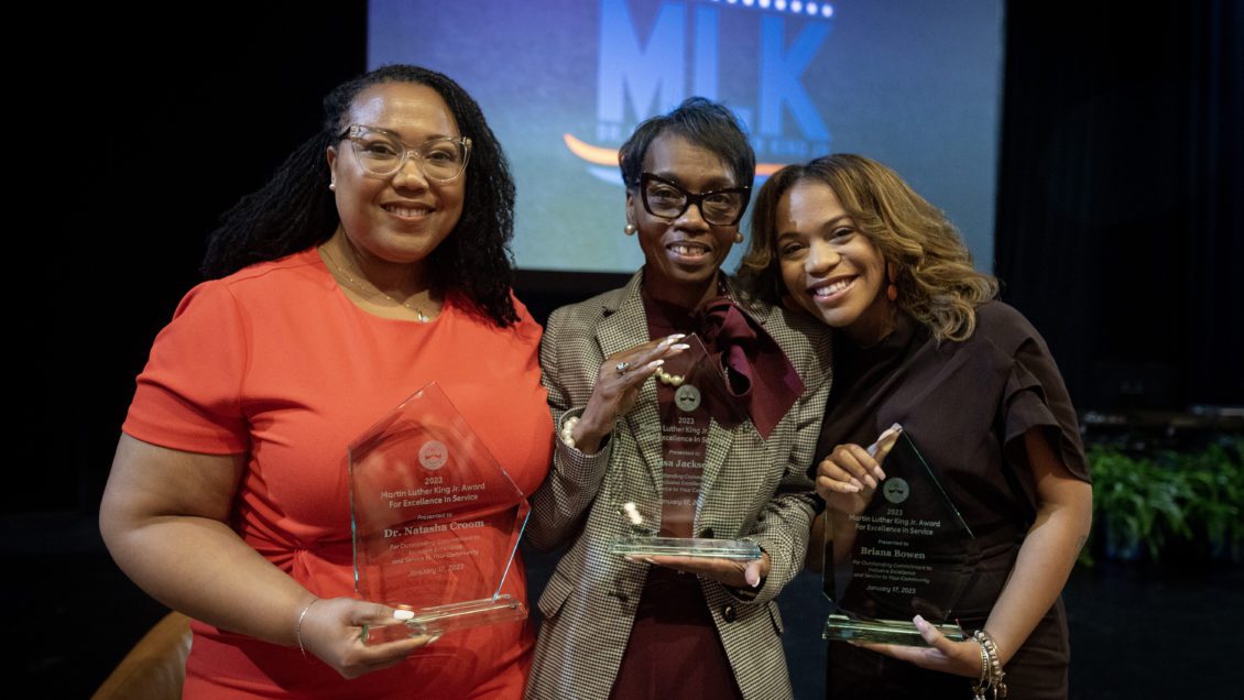 Three women hold glass awards and smile at the camera