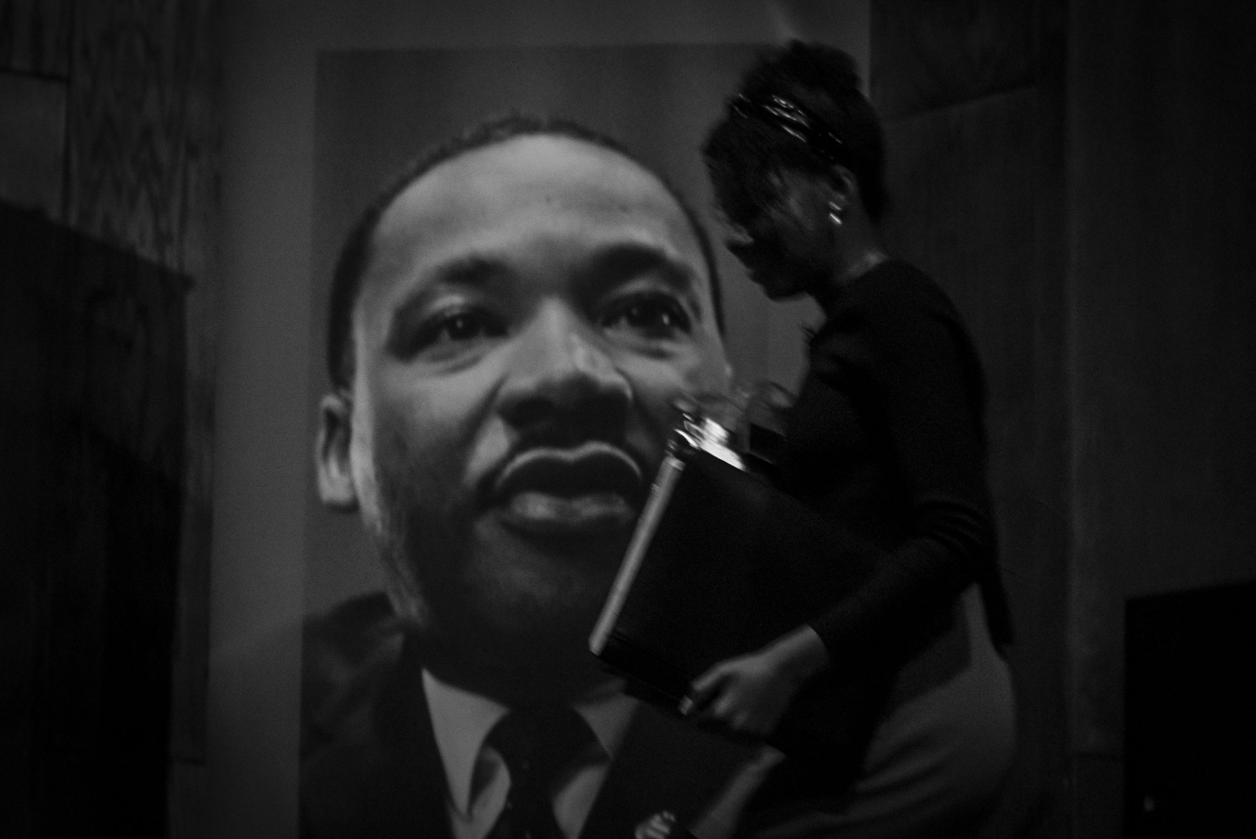 Black and white image of a young woman - Yolanda King - walking past a large poster of MLK.