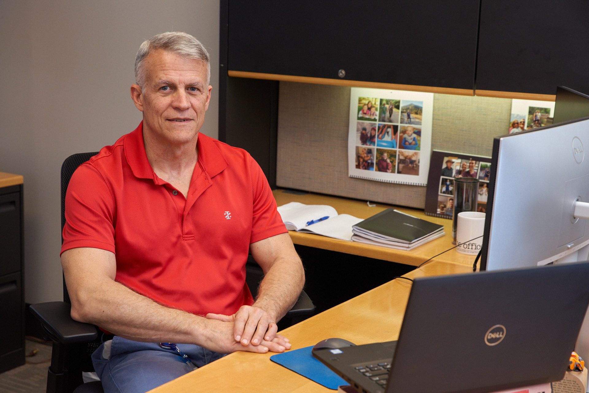 A man wearing a red shirt sits at a desk.