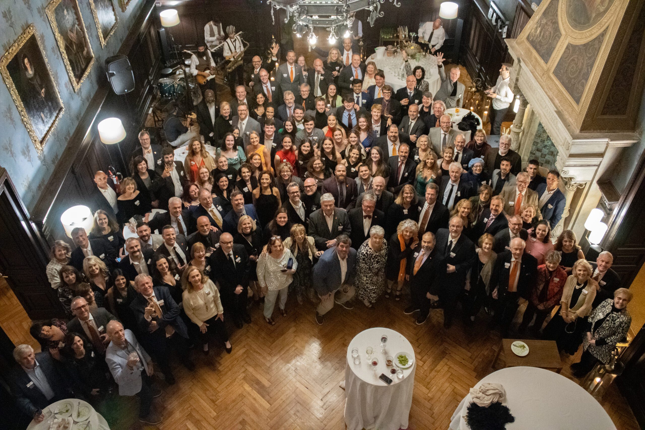 A group of more than 100 formally-dressed Clemson architecture alumni and students smile up at the camera from the floor of an ornate ballroom.