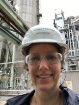 Woman in hard hat standing in front of an industrial building