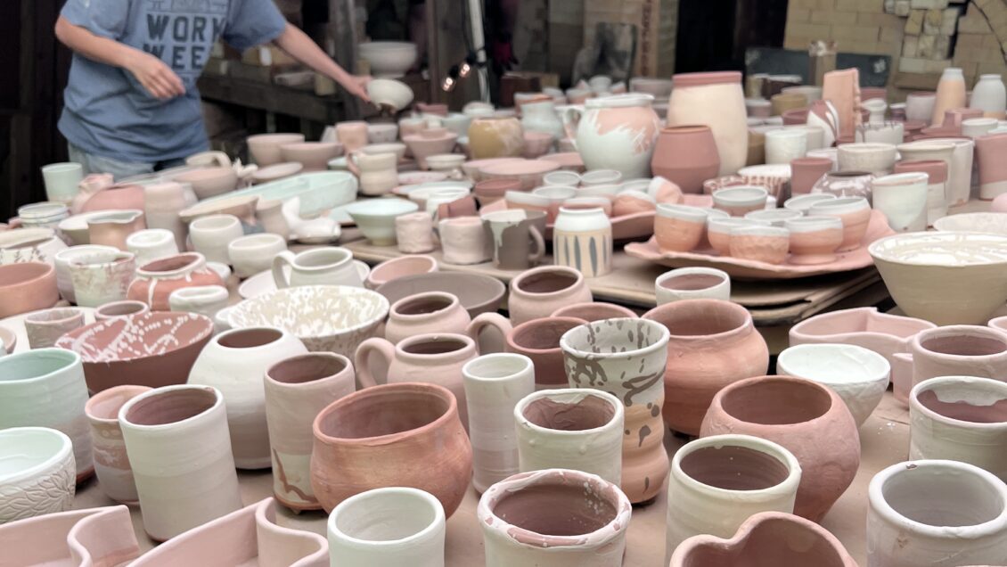 A large table is covered with ceramic work that is ready for the kiln.