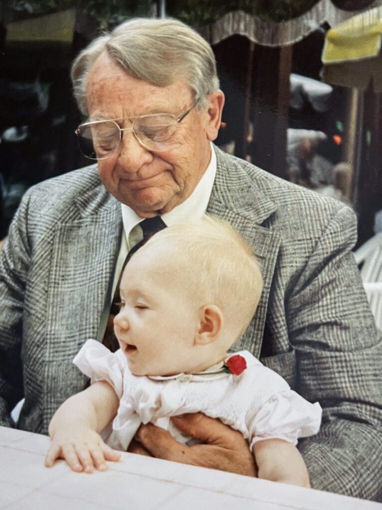 A smiling man sits at a table with a laughing baby in his lap.
