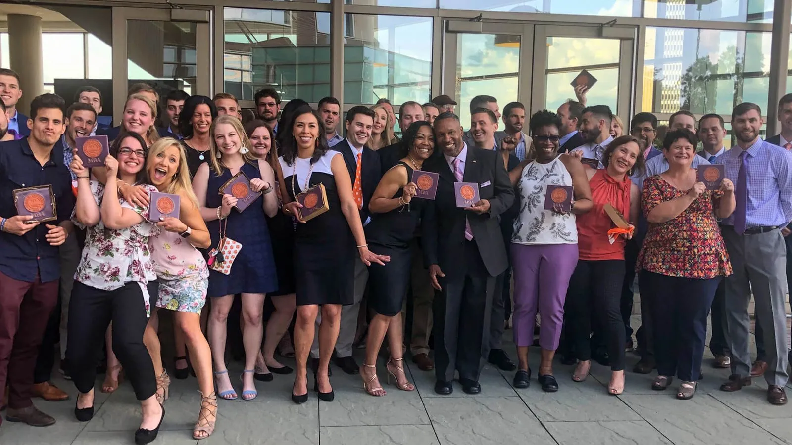 A group of MBA students gather in front of the Greenville One building to celebrate their upcoming graduation from a school with a best graduate schools ranking