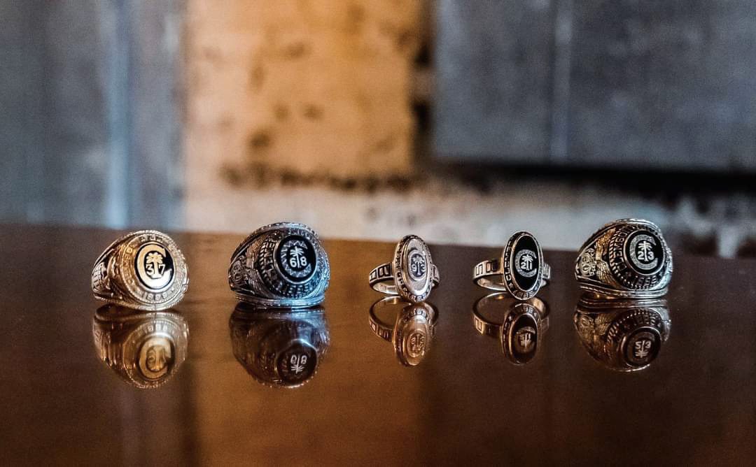 Five Clemson class rings sit in a row on a table top