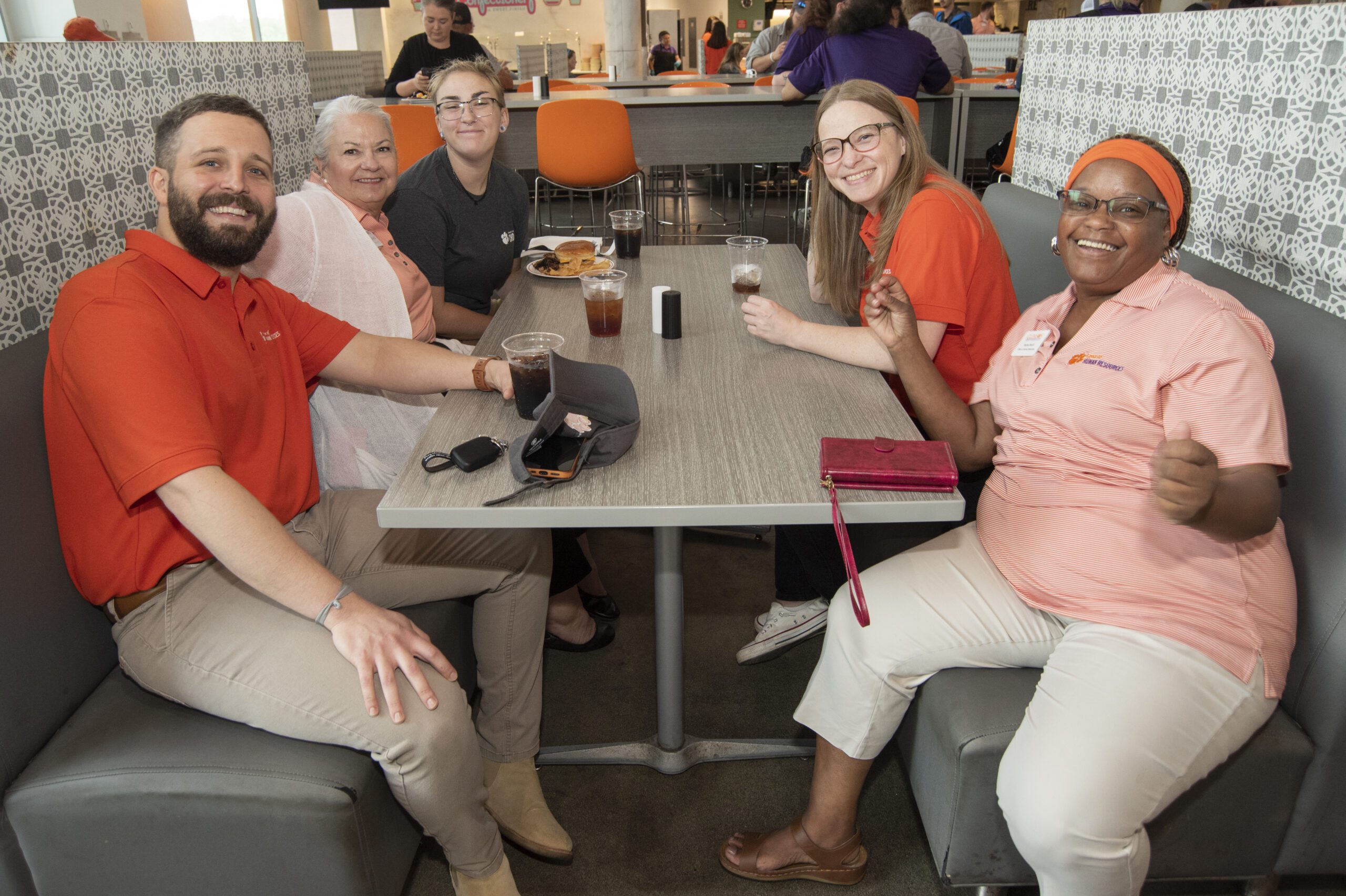 Five coworkers, wearing various Clemson apparel, sit at a booth and smile for a photo.