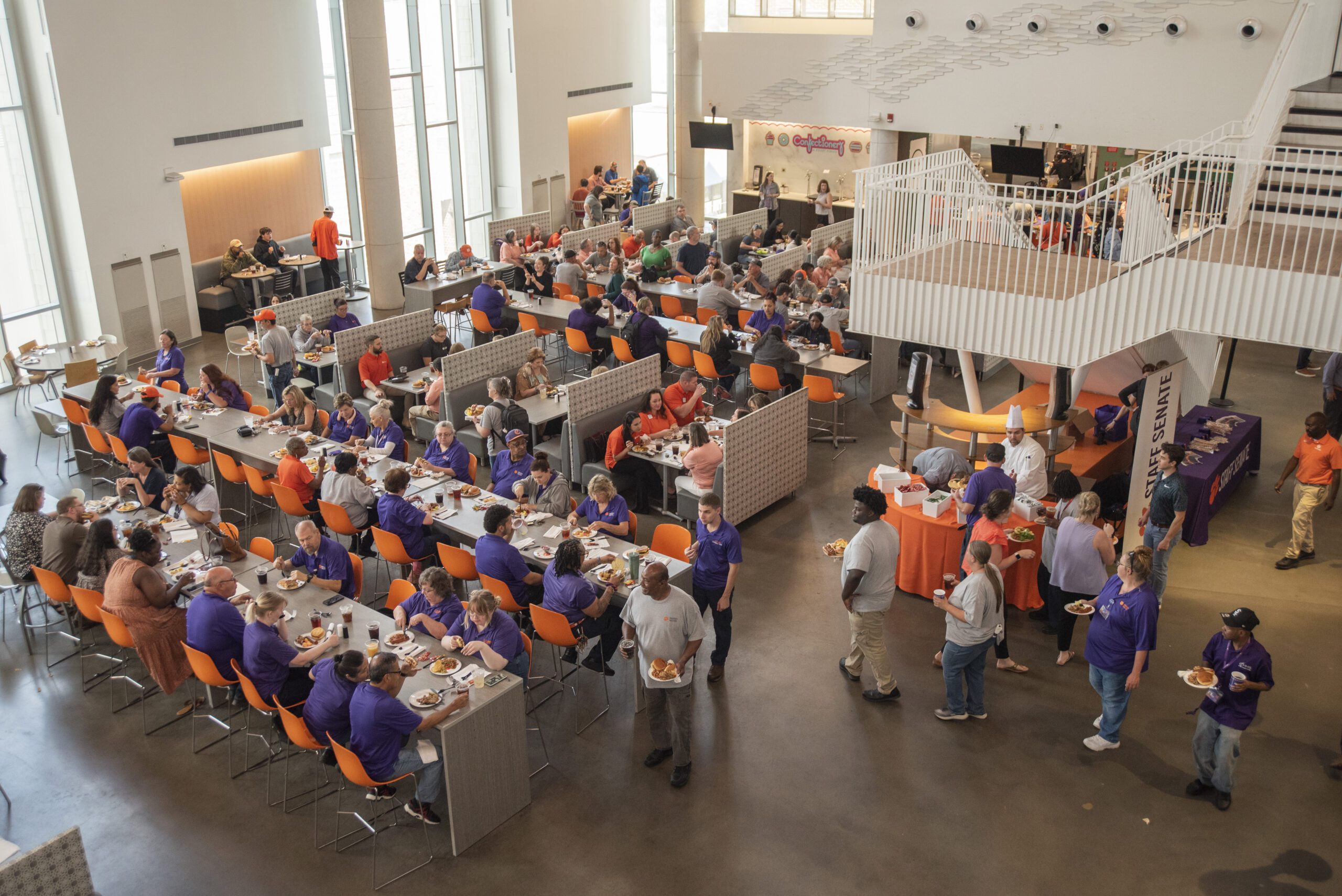 Arial view of people sitting around tables and walking around a dining hall with plates of food.