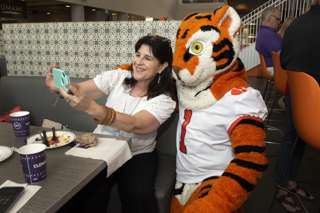 A woman holds an iPhone up to take a selfie with the Clemson Tiger mascot.
