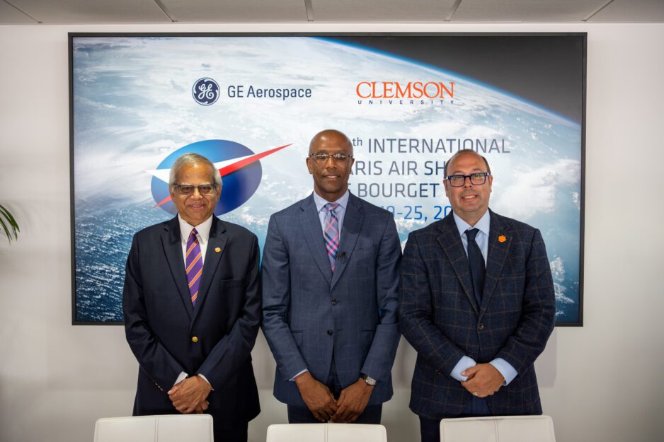Three men wearing suits are seated in front of a Paris Air Show GE Aerospace and Clemson University banner