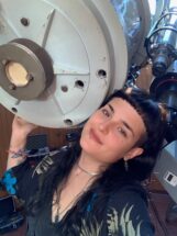 A woman with black hair in front of a telescope.