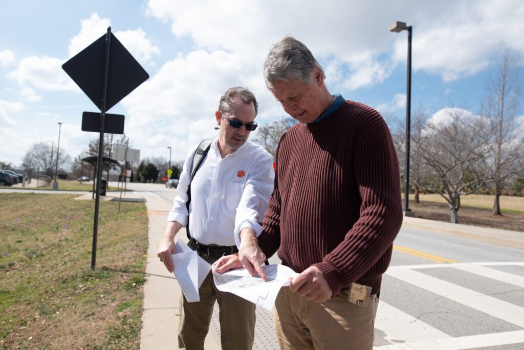 Two men stand on a sidewalk looking at a map