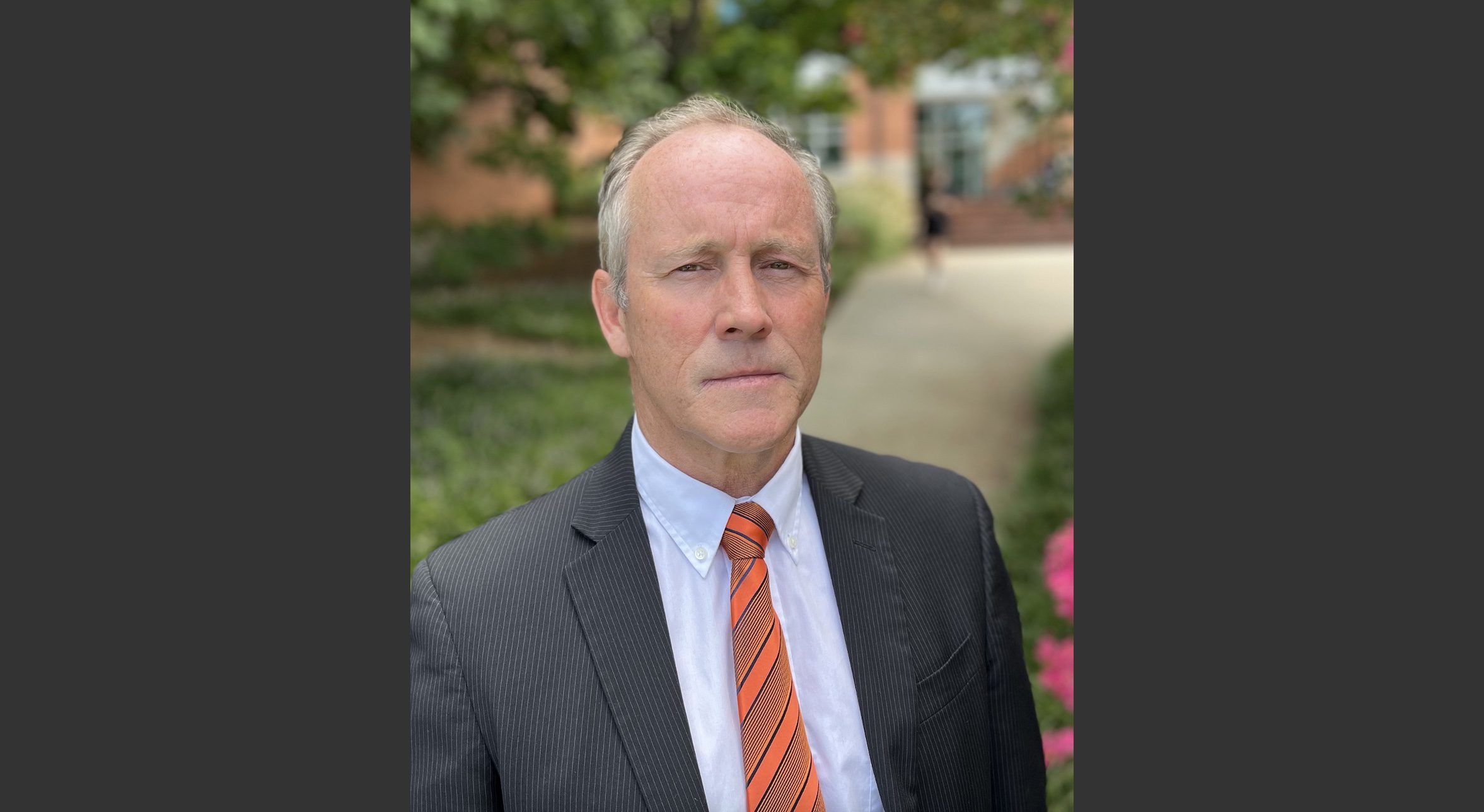 Professional man in grey suit and orange tie standing in front of university buildiing.