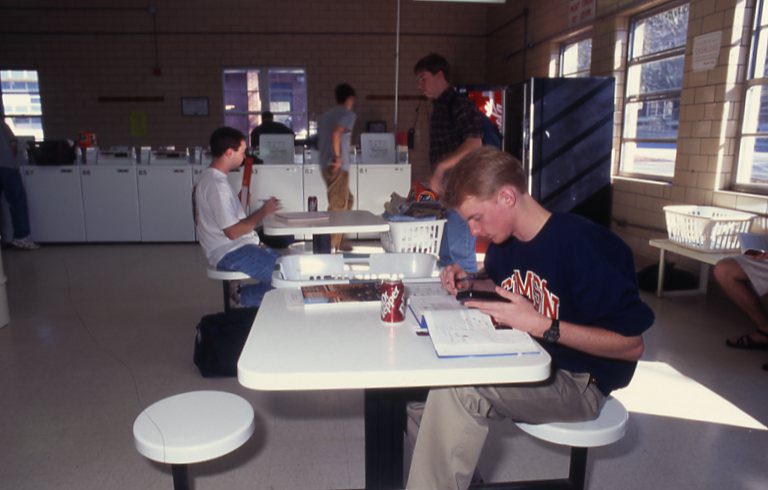 A student in the 1990s or early 2000s studies at a table with laundry machines surrounding him in the Dillard Building 