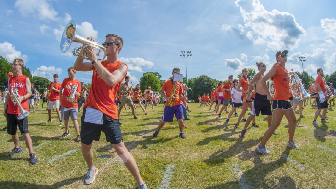 A trumpeter practices some choreography with other members of the marching band on a beautiful sunny day