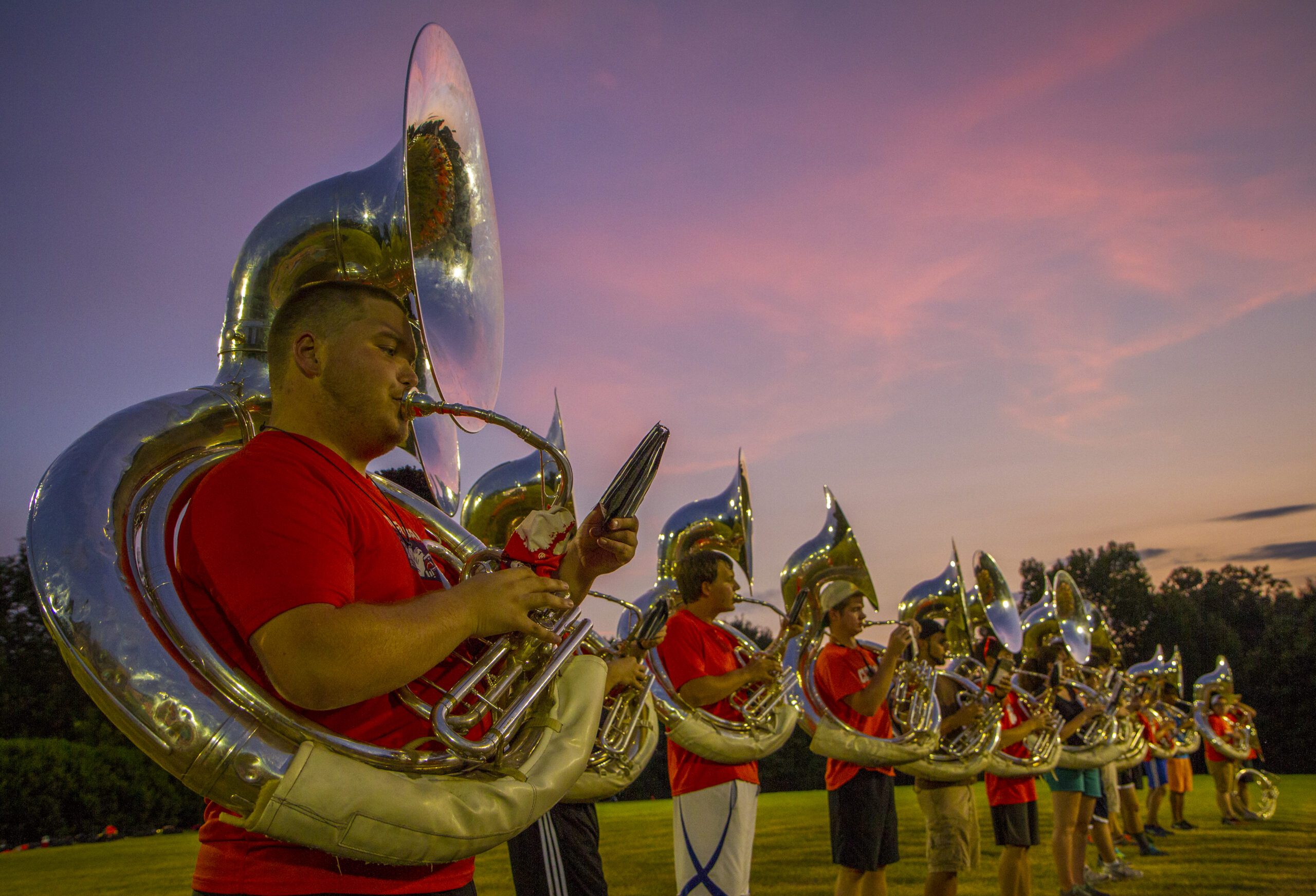 A row of sousaphone players rehearse under a bright orange sunset