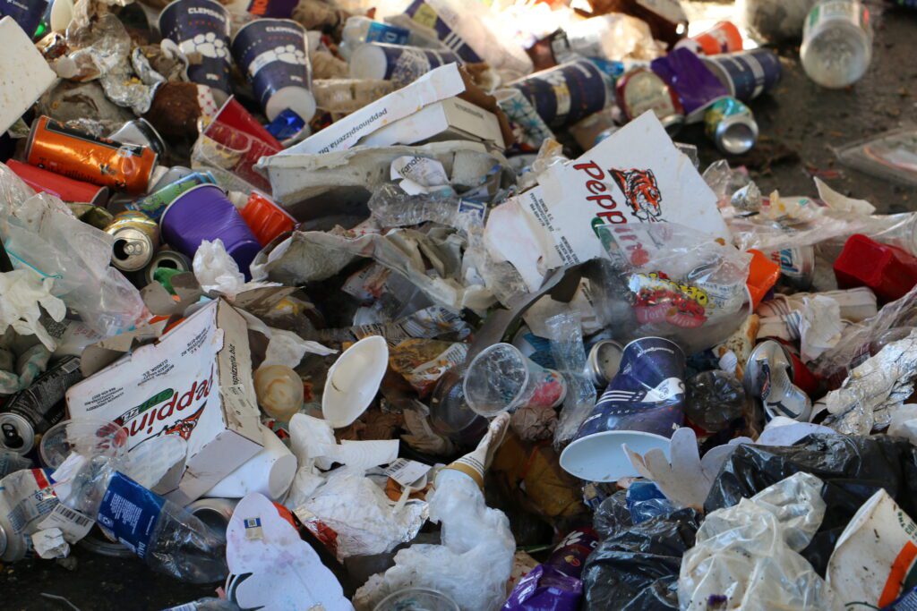 a mound of trash, consisting of pizza boxes, paper products, plastic cups, aluminum cans, ice bags and other discarded items one might find after tailgating at a sporting event. Some which can not be recycled. 