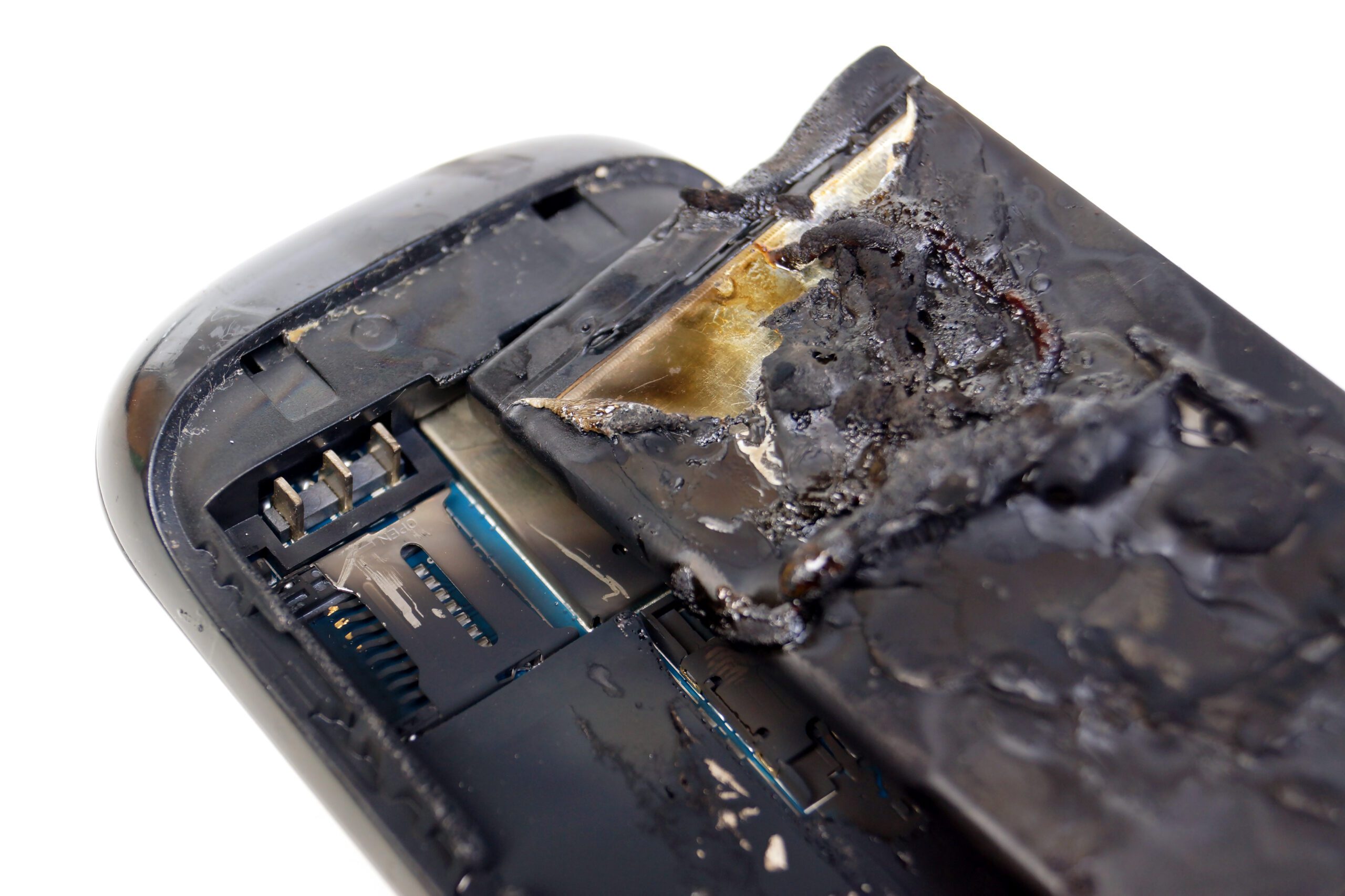A black cell phone is in pieces, pictured from the back with fire damage.
