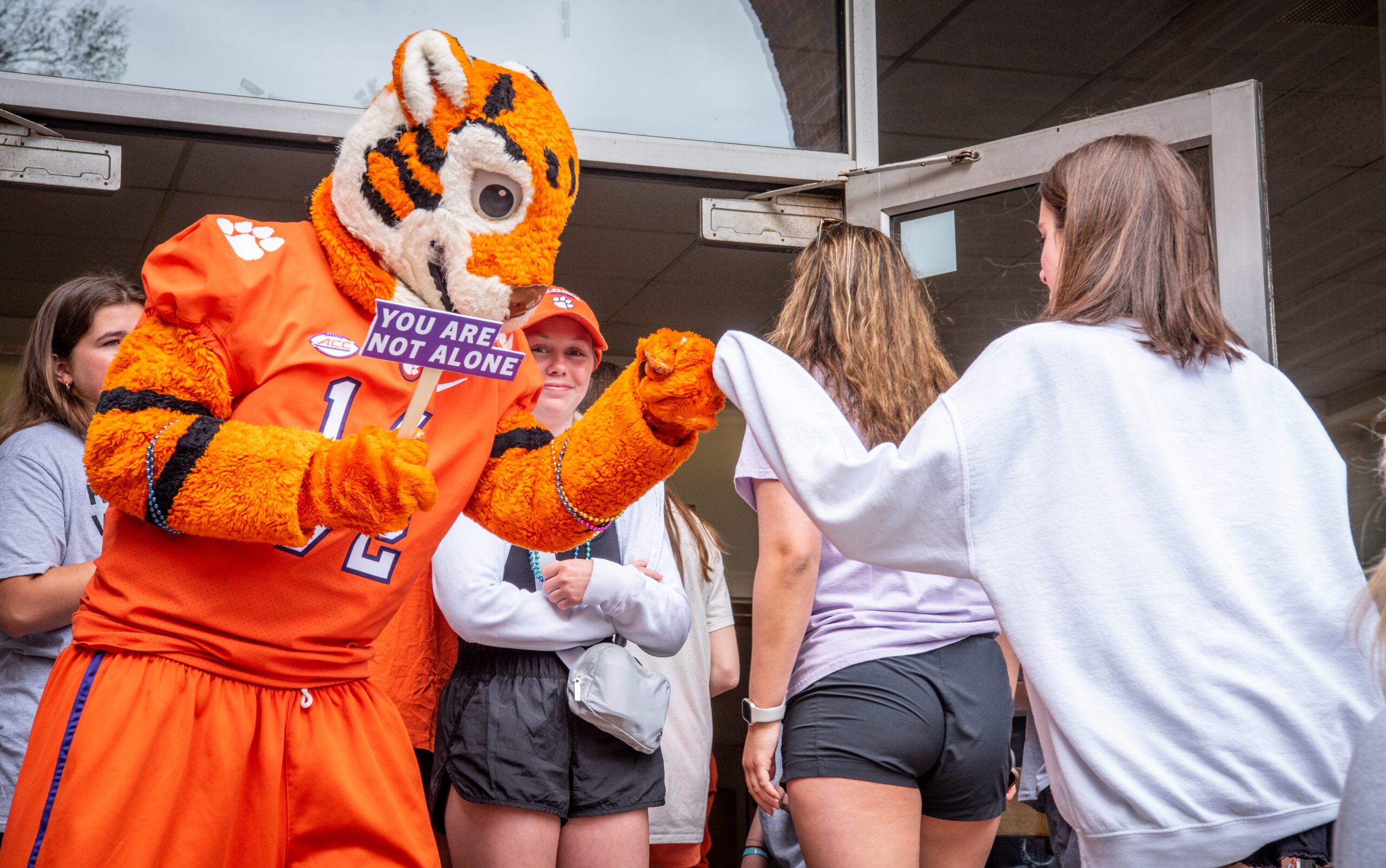 The Clemson Tiger fist-pumping with a student while holding a sign that says "You Are Not Alone"