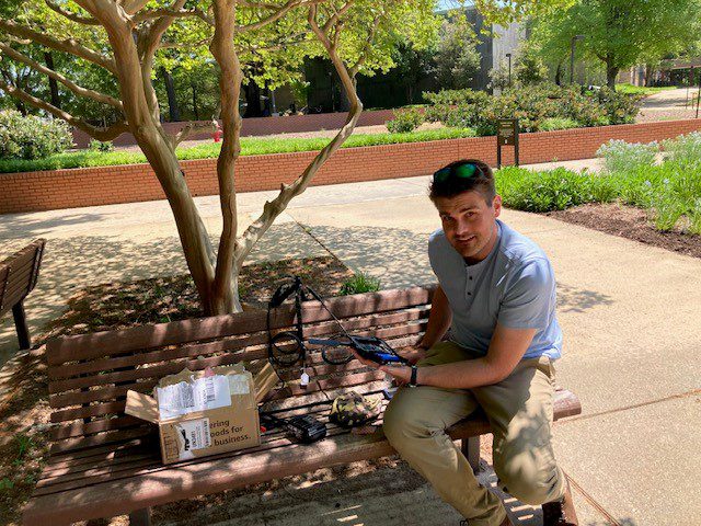 Jeremy Dertien, Ph.D., sits on a bench holding the TrailGuard AI technology.