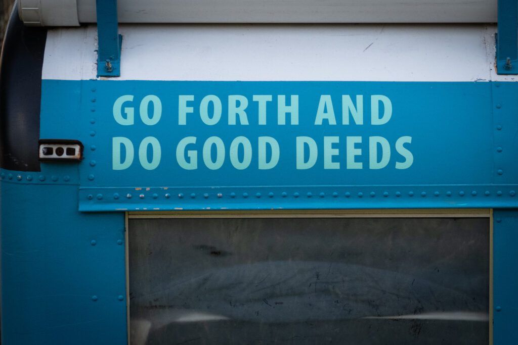 The words "Go forth and do good deeds" painted above the window of a bus.