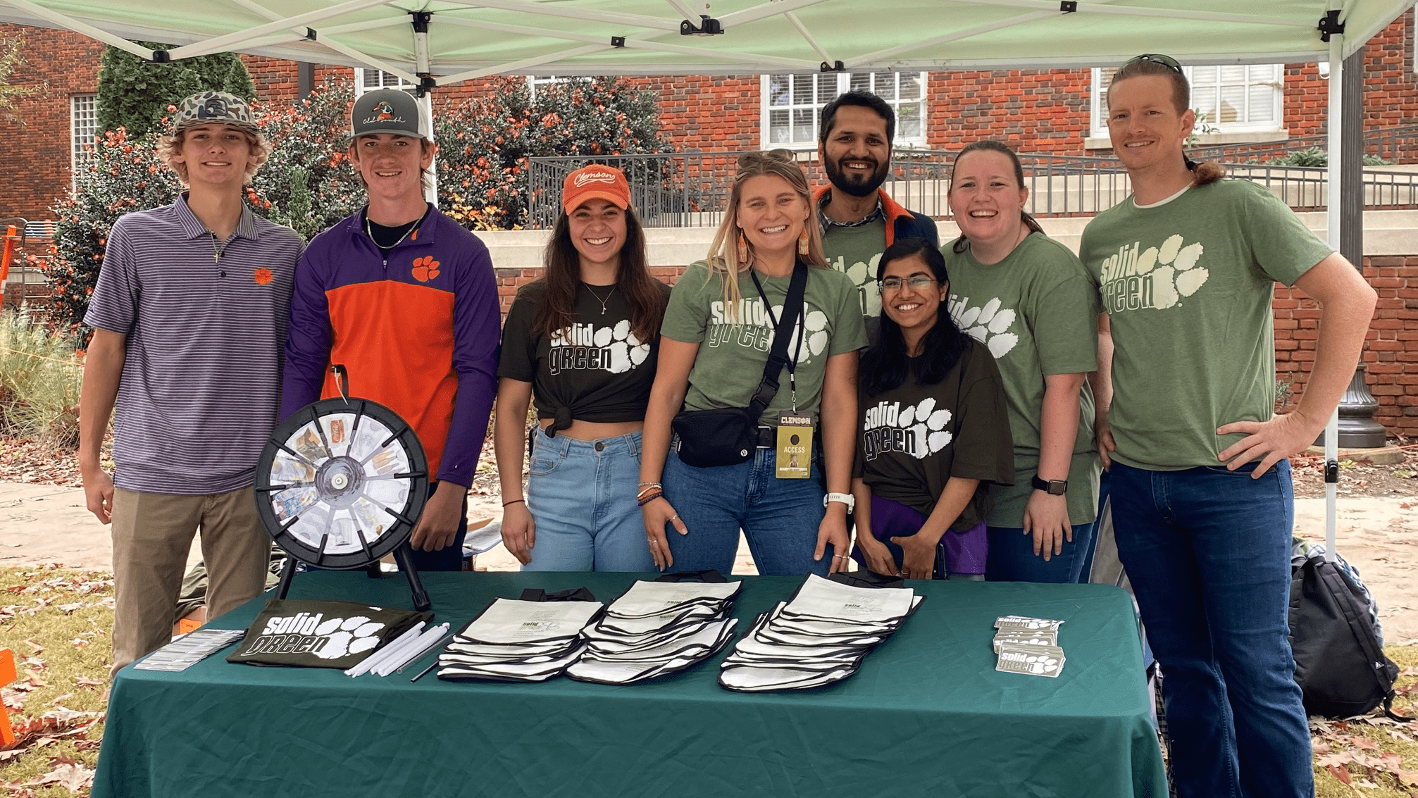 Clemson students from the Solid Green program pose under a green tent behind a green table with giveaway items