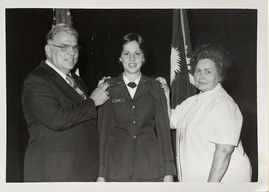A black-and-white photo from the 1980s where a woman in Air Force dress blues receives congratulations from an older man and an older woman