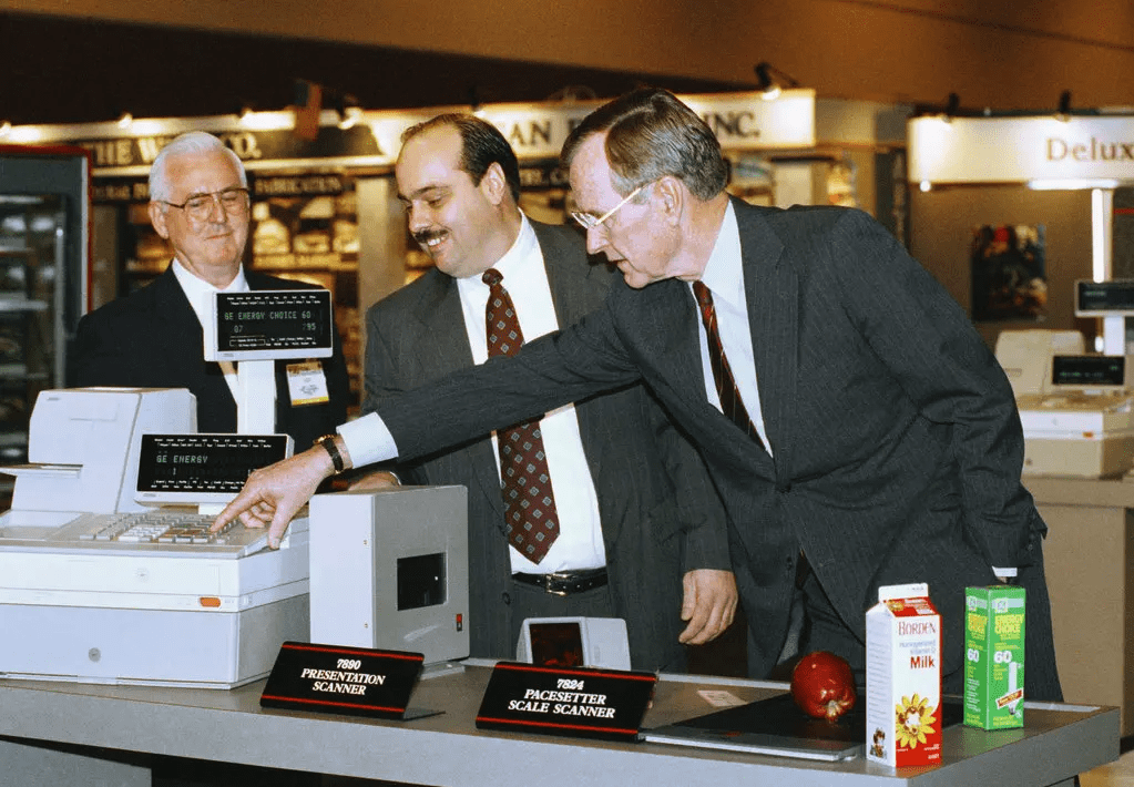 President George H.W. Bush leans over and points at a cash register.
