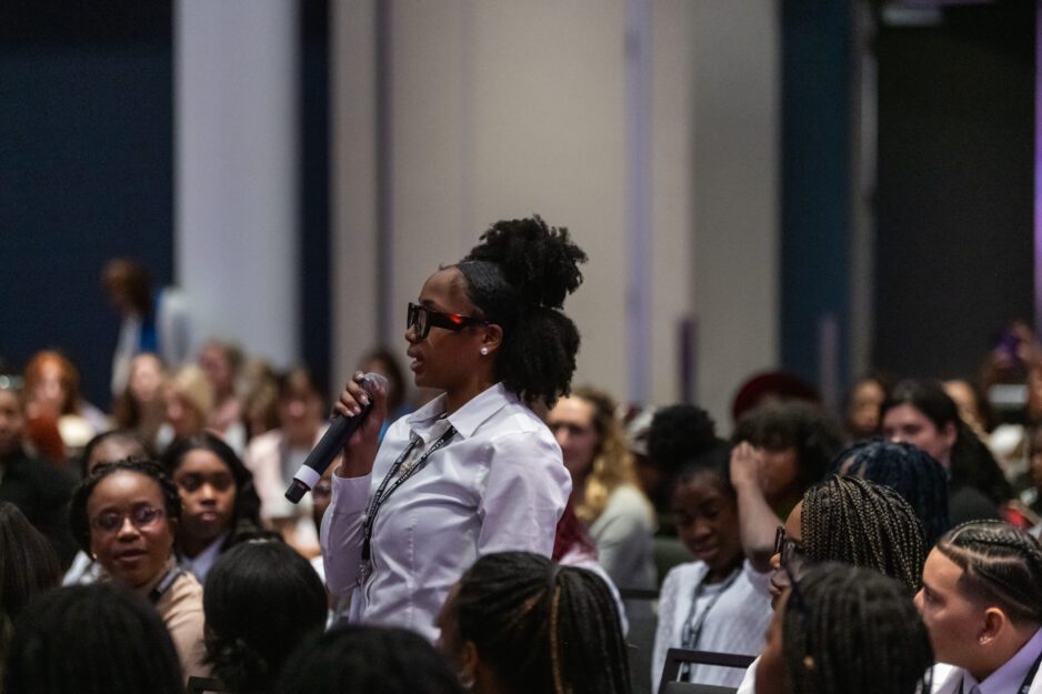 A photo of Paige Felder standing in the crowd and speaking into a microphone.