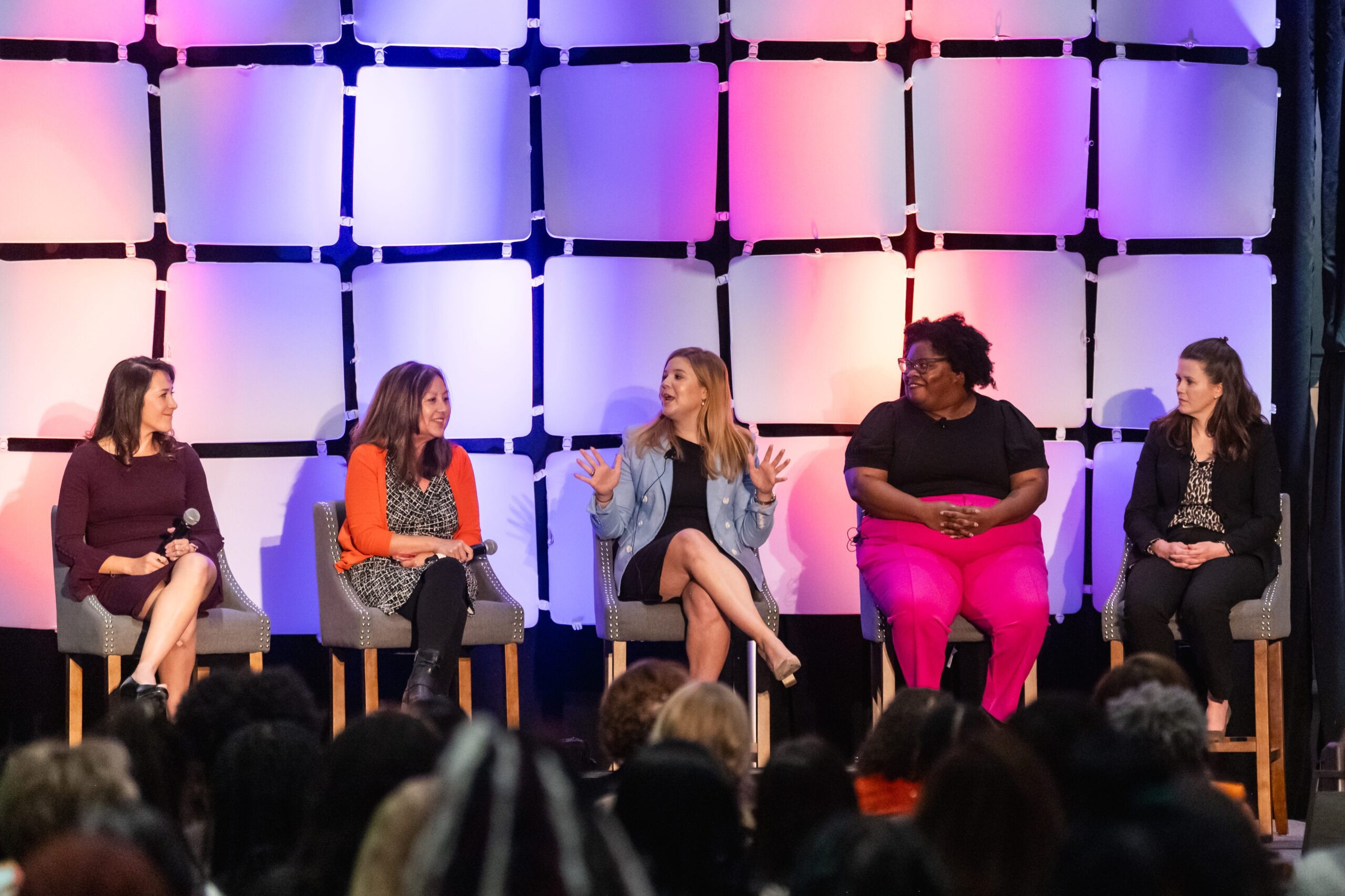 Five women sit in high stools on a stage during a panel discussion.