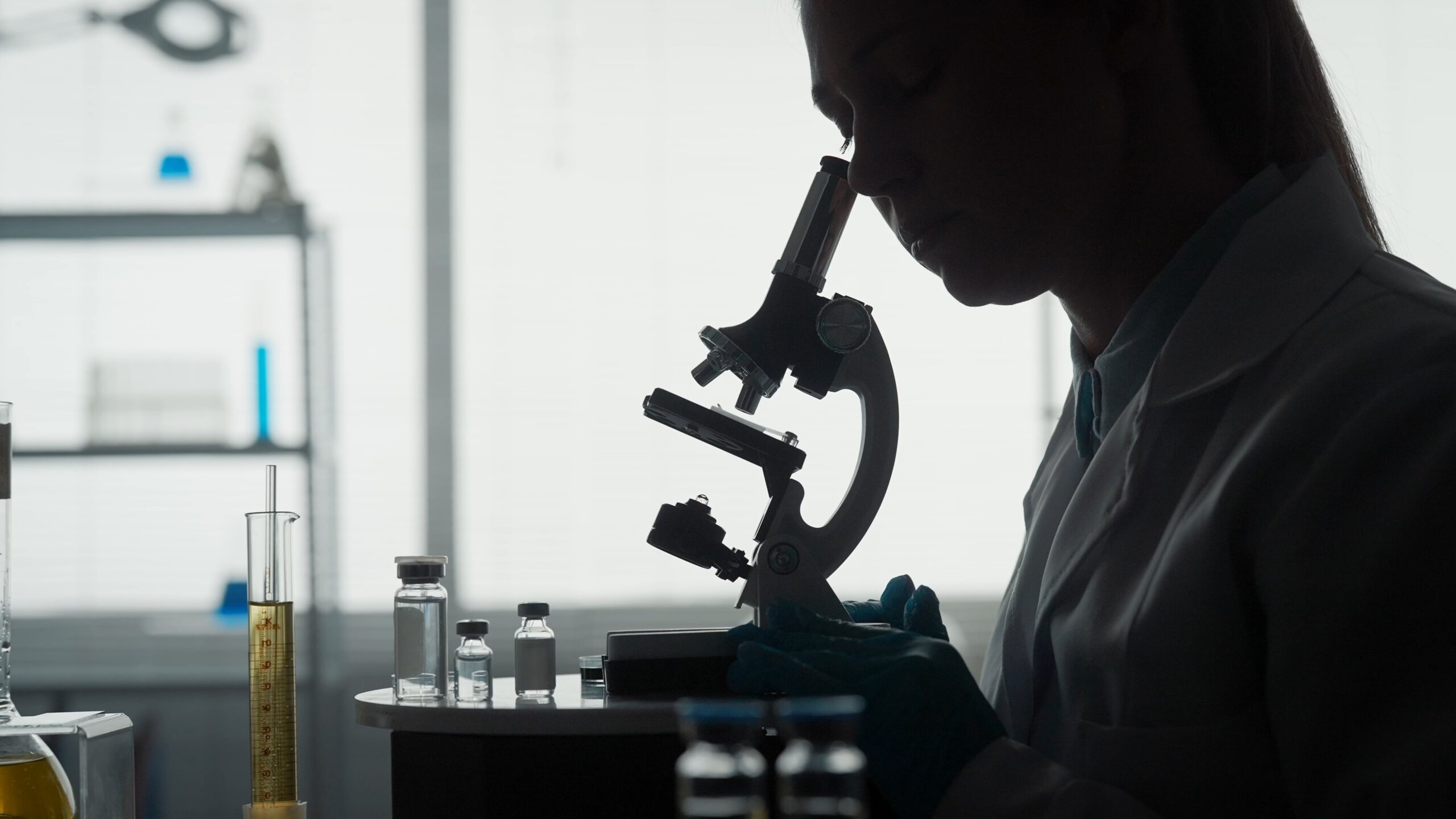 Silhouette of a woman looking into a microscope in a science lab.