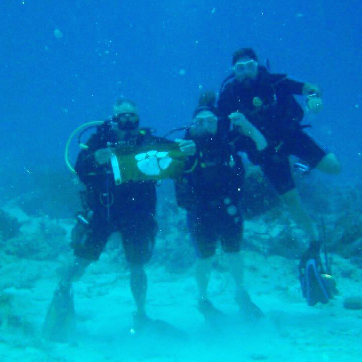 Three people scuba diving, holding Clemson Tiger Rag