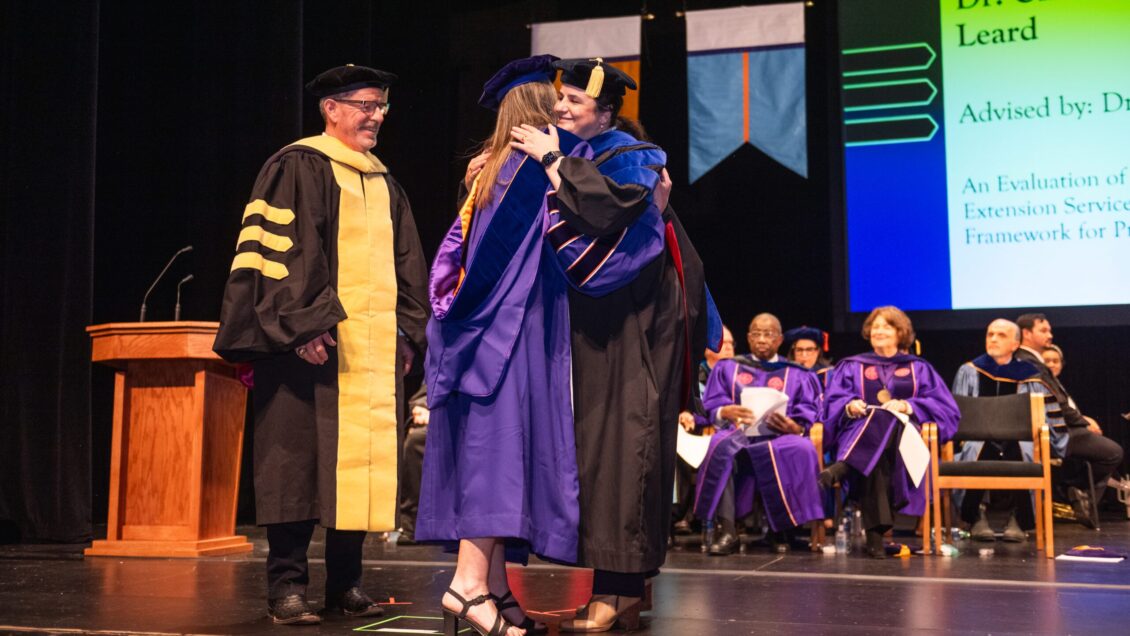 Doctoral graduate is greeted by college leadership on stage
