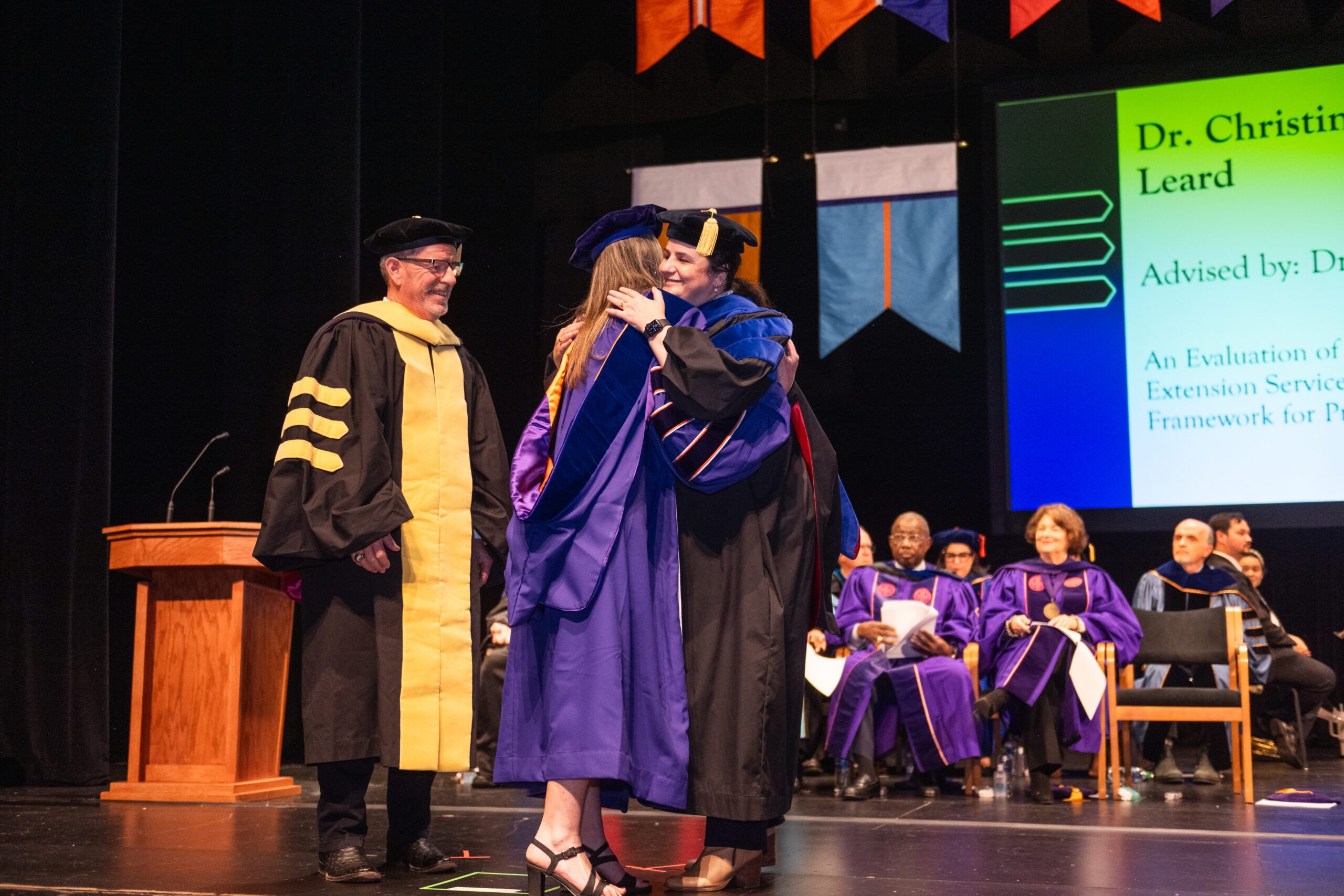 Doctoral graduate is greeted by college leadership on stage