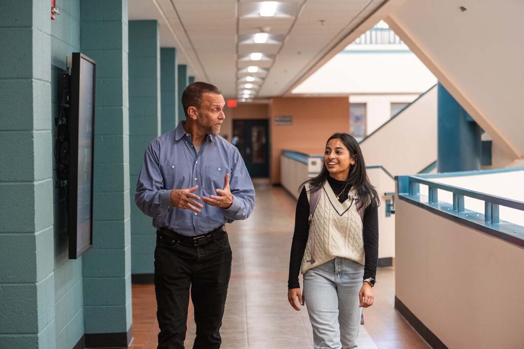 Psychology professor Robert Sinclair and Shreya Tellur walking together down a hallway in Brackett Hall. 