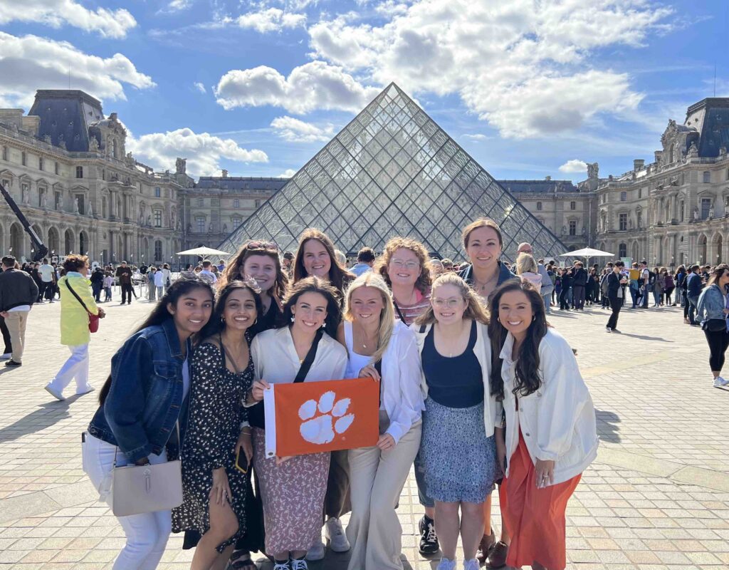 Shreya Tellur (bottom row, second from left) and other members of her Dixon Global Policy Scholars cohort posing with a Tiger Rag in front of the Louvre Museum. 