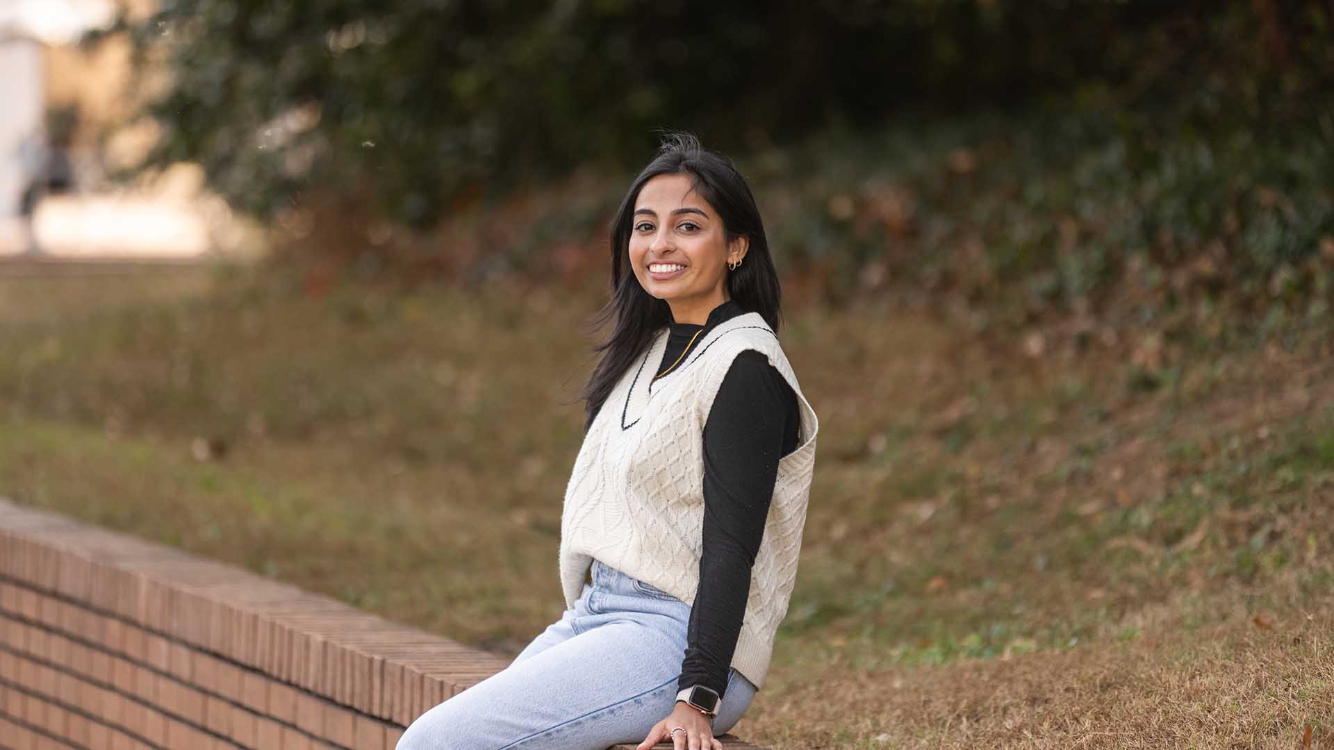 Psychology major Shreya Tellur leaning against a brick wall by the Reflection Pond on Clemson University campus.