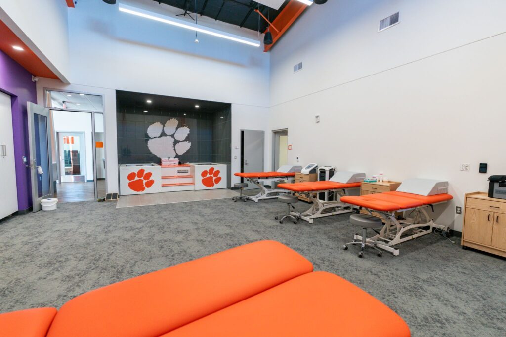 A large room with Clemson Tiger Paws on the wall and orange athletic training tables