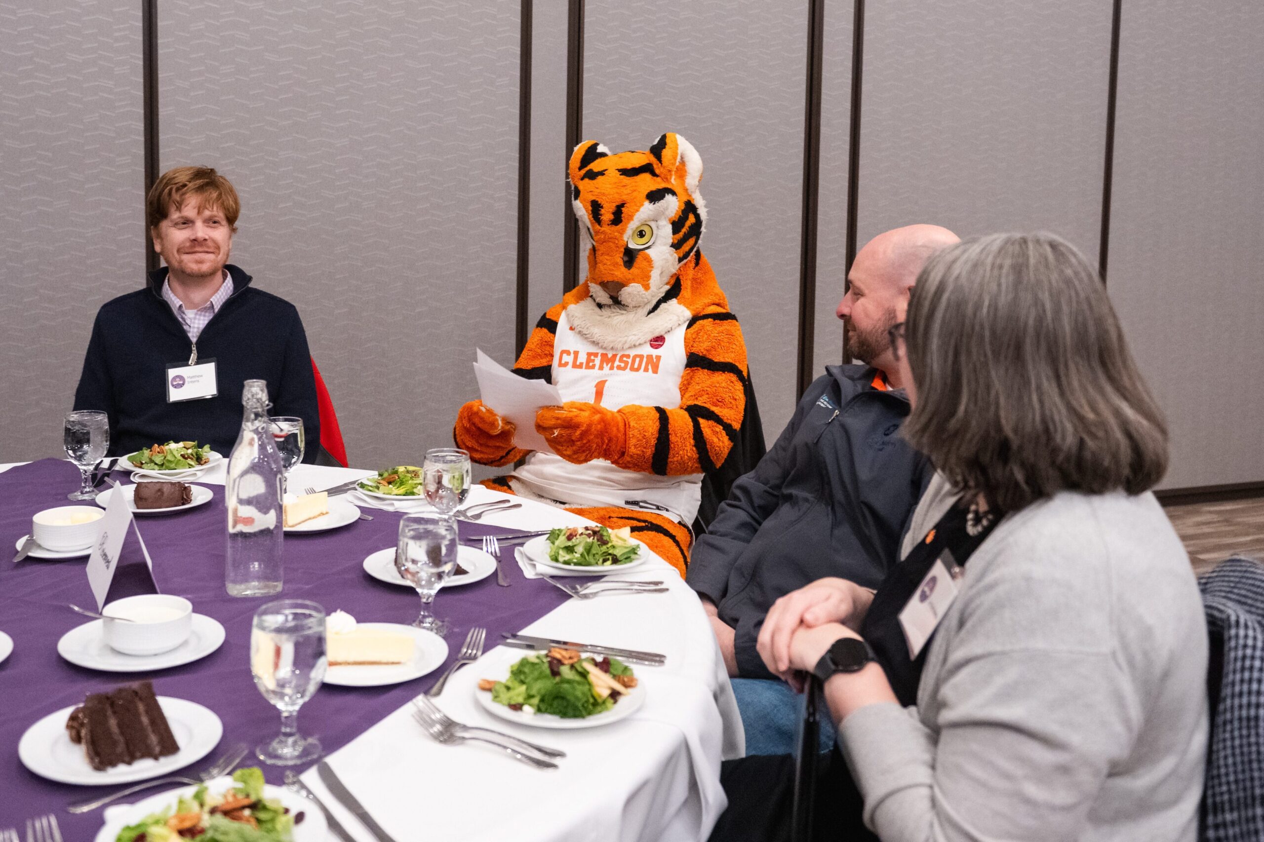 The Clemson Tiger mascot sits at a lunch table surrounded by employees.