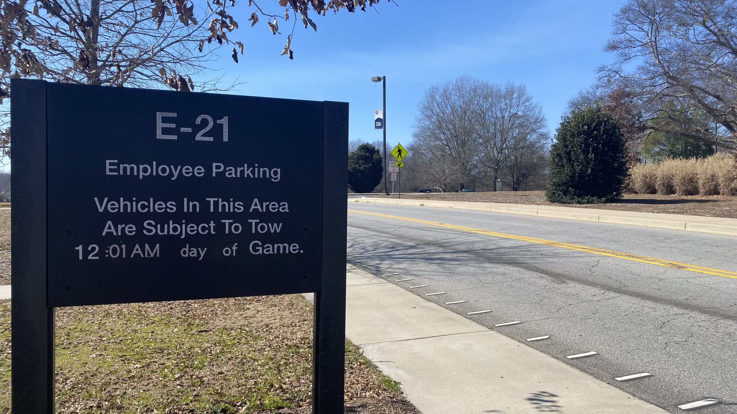 A roadsign sign reading "E-21 Employee Parking Vehicles in this area are subject to tow 12:01 AM day of game"