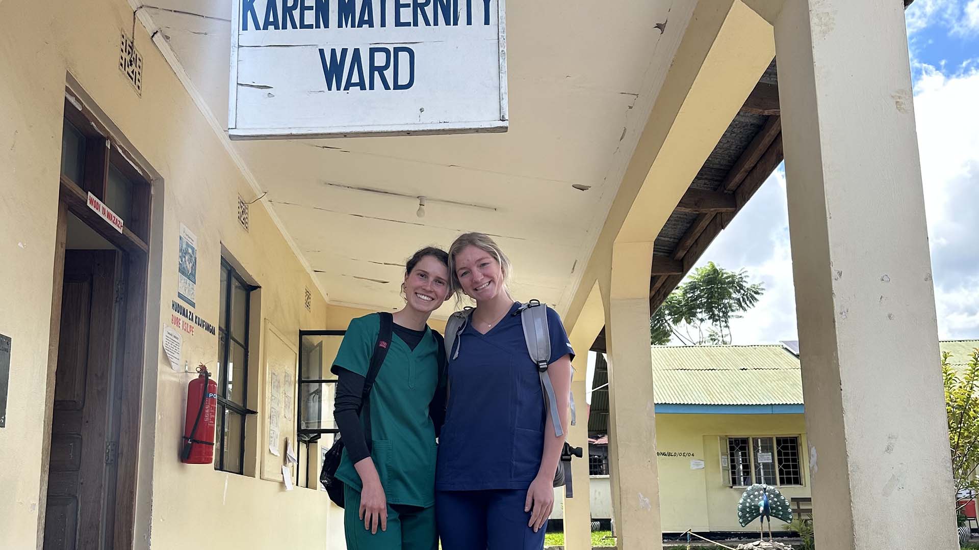 Two women in nurse’s scrubs standing beside the entrance to a maternity ward in Arusha, Tanzania.