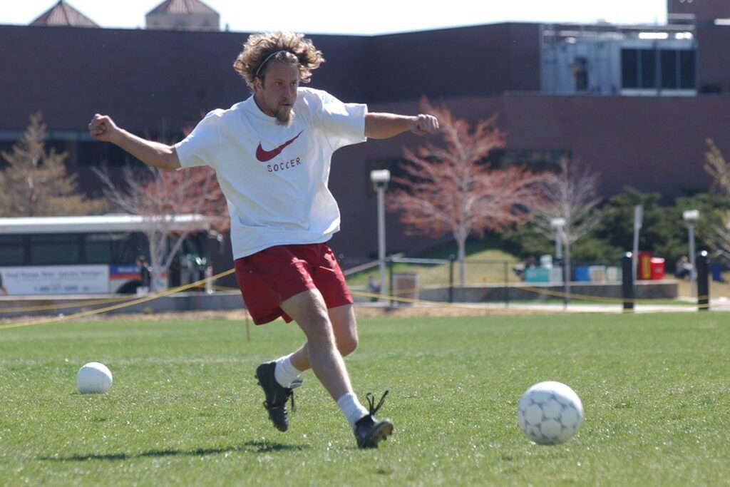 Josh Blue kicks a soccer ball on a practice field.